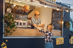 Food Truck Employee Hands Out a Freshly Made Burger and a Soft Drink to a Happy Young Female. Street Food Truck Selling Burgers in a Modern Hip Neighbourhood